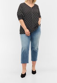 Svart blus med vita prickar, V-ringning och knappar, i kombination med ljusblå cropped jeans och svarta klackskor. Slät tygtextur.