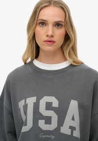 Grijze sweatshirt met grote "USA" grafiek in lichtgrijs. Heeft een relaxte pasvorm en ribbelkraag, gemaakt van zachte, gestructureerde stof.
