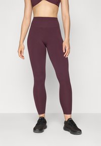 Bordeaux hoge taille leggings van rekbare stof, met een gladde textuur. Gecombineerd met zwarte sportschoenen voor een complete look.