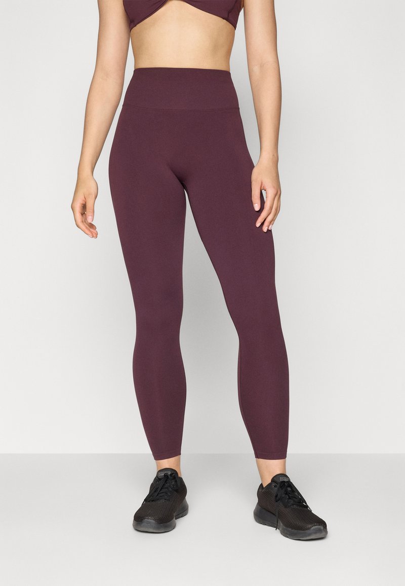Bordeaux hoge taille leggings van rekbare stof, met een gladde textuur. Gecombineerd met zwarte sportschoenen voor een complete look.