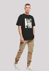Sort bomulds t-shirt med grafisk print af et ansigt, parret med khaki cargo bukser og hvide sneakers. Casual fit, korte ærmer.