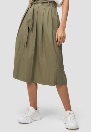 Jupe midi vert olive avec des plis et une ceinture nouée à la taille, portée avec des baskets blanches épaisses sur un fond clair.
