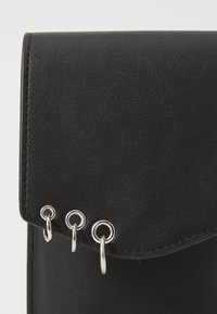 Black faux leather clutch with a smooth texture, triangular flap, and three silver hardware rings along the edge.