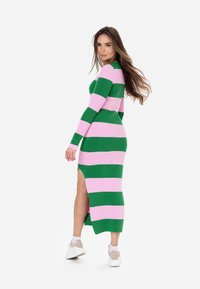 Abito longuette aderente caratterizzato da ampie strisce orizzontali verdi e rosa, con uno spacco laterale e una texture a costine. Indossato con sneakers bianche.