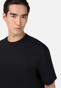 Černé tričko s krátkým rukávem a kulatým výstřihem, vyrobené z hladké látky, s klasickým střihem a minimalistickým designem.