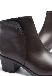Botas de tobillo de cuero marrón con una textura suave, tacón bajo y apilado, y un diseño minimalista. Presentan costuras limpias y paneles laterales elásticos.