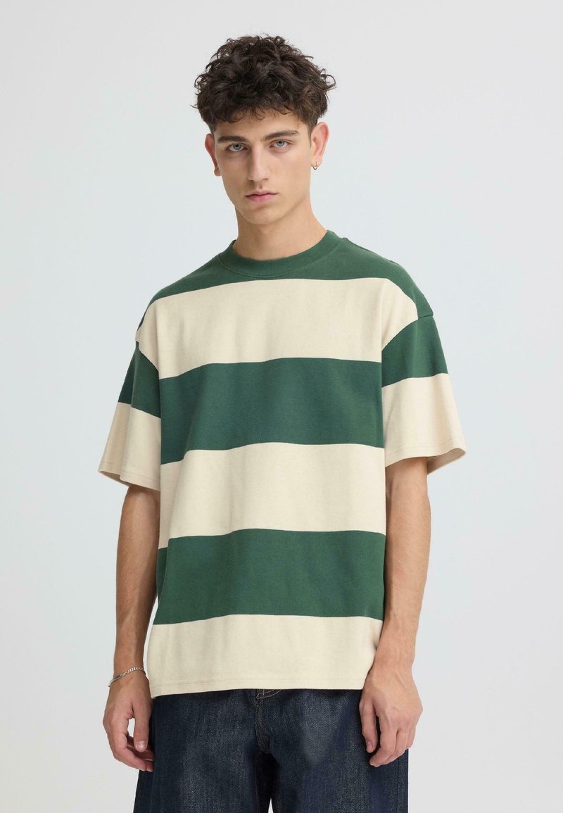 T-shirt à manches courtes rayé vert et beige, fabriqué en tissu doux avec une coupe décontractée et un col rond, porté avec un jean foncé.