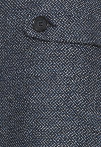 Modrý a černý strukturovaný materiál s tkaným vzorem, s detailem černého plastového knoflíku na hladkém povrchu.