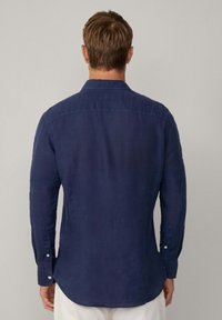 Navy blue long-sleeve shirt made of textured fabric, featuring a standard collar, button cuffs, and a curved hem, viewed from the back.