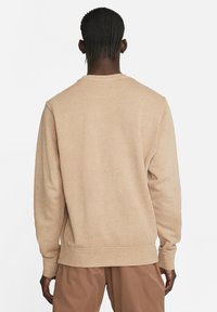 Beige sweater made of textured fabric, featuring a round neckline, long sleeves, and ribbed cuffs. The back is smooth with flecks visible.