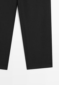 Pantalon noir coupe droite posé à plat montrant les parties basses des jambes et les ourlets sur fond blanc.