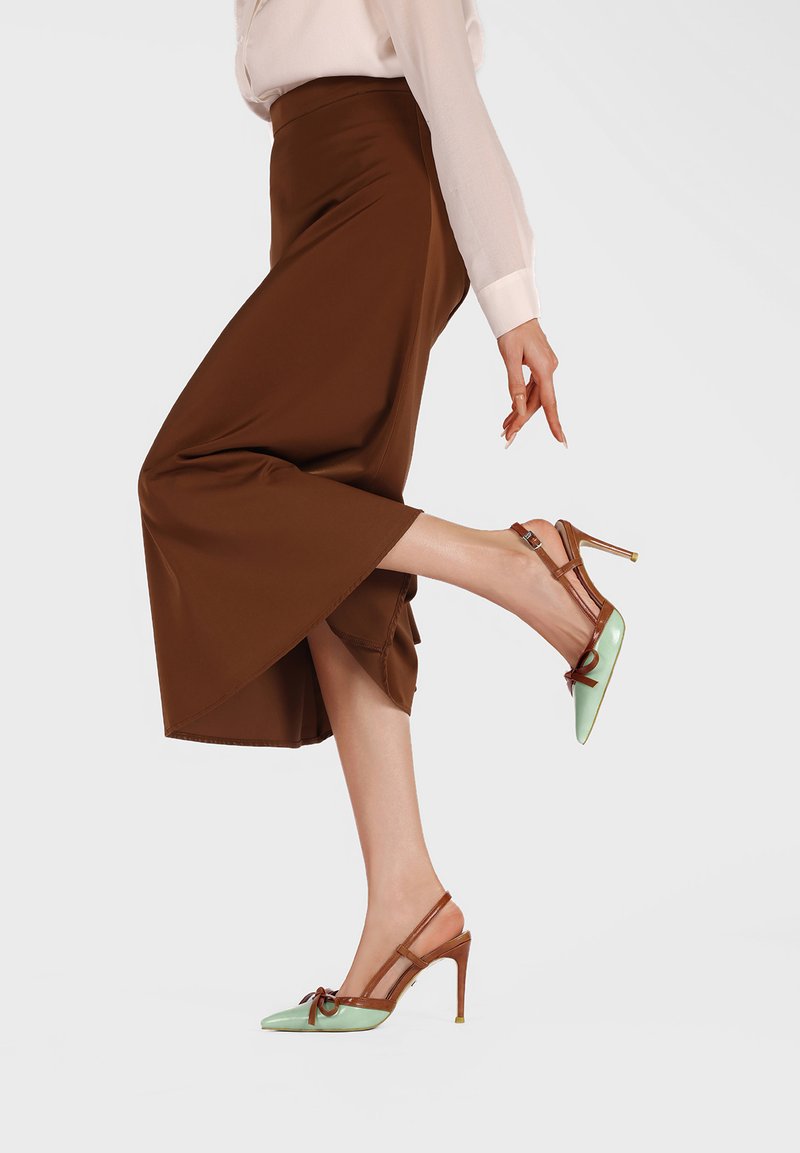 Femme portant une jupe midi marron et des escarpins slingback à bout pointu vert menthe avec des brides marron, levant un pied derrière elle.