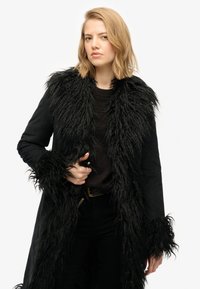 Sort frakke med faux fur krave og manchetter, der har en tekstureret overflade. Designet med en lang silhuet og åben front.