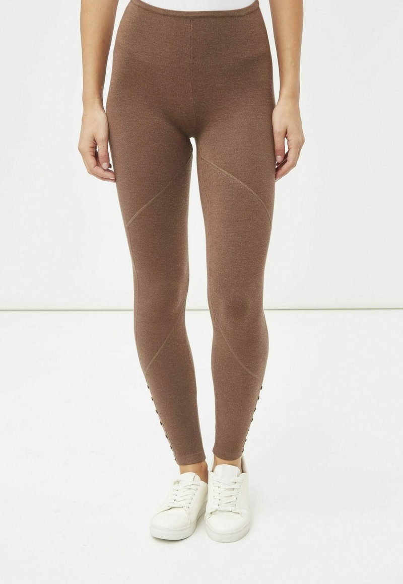 Leggings marrones de tela elástica, con una cinturilla alta, paneles texturizados y detalles de botones laterales, combinados con zapatillas blancas.