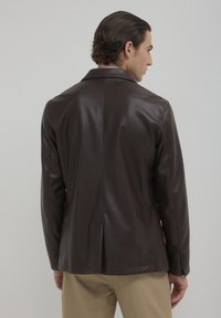 Blazer marrone in finta pelle con una vestibilità su misura, colletto a revers e polsini con bottone, dotato di una fessura singola sul retro per una maggiore flessibilità.