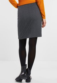 Spódnica z mieszanki wełny w wzór jodełki, w kolorze szarym i czarnym, sięgająca powyżej kolan, zestawiona z czarnymi rajstopami i botkami na kostkę.