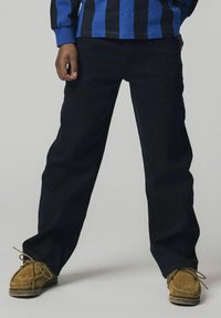 Los jeans negros de pierna recta tienen un diseño sencillo con costuras sutiles. Se combinan con zapatos de ante marrón que tienen cordones y textura contrastantes.