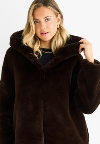 Brown faux fur hooded coat with a plush texture, wide sleeves, and a deep V-neck collar. The fabric exhibits a soft, fluffy appearance.