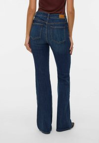 Jeans de mezclilla azul acampanados con cintura de talle medio, que cuentan con dos bolsillos traseros y una etiqueta de cuero en la pretina. Textura suave, con mínimo desgaste.