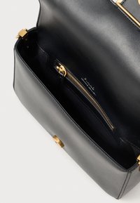 Interior de uma bolsa de mão de couro preto com uma textura suave, hardware em tom dourado e um bolso com fecho para organização.