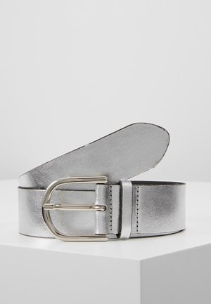 Cinturón de cuero metálico plateado con una hebilla redondeada dorada, enrollado sobre una superficie blanca contra un fondo gris claro.