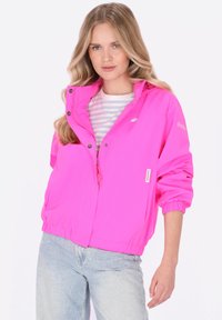 Růžová lehká bunda se zipem vpředu, patentními knoflíky a elastickými manžetami. Spárována s pruhovaným tričkem a světlými modrými džínami.
