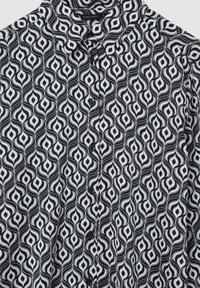 Camicia a righe bianco e nero con un design vorticoso, colletto classico e chiusura a bottoni. Tessuto morbido e leggero.