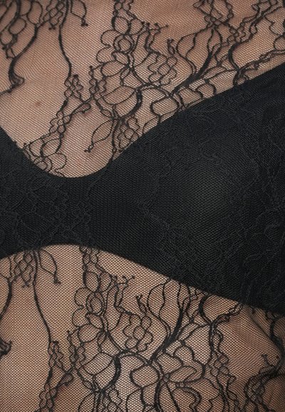 Țesătură din dantelă neagră cu modele florale suprapuse pe o nuanță de piele nude, evidențiind detaliile intricate ale textilului și contrastul dintre dantelă și materialul solid negru.