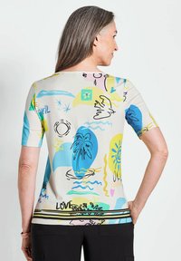 Kurzarmshirt aus weichem Material mit abstrakten Mustern in Blau, Gelb, Pink und Schwarz auf einem hellen Hintergrund; mit rundem Halsausschnitt.