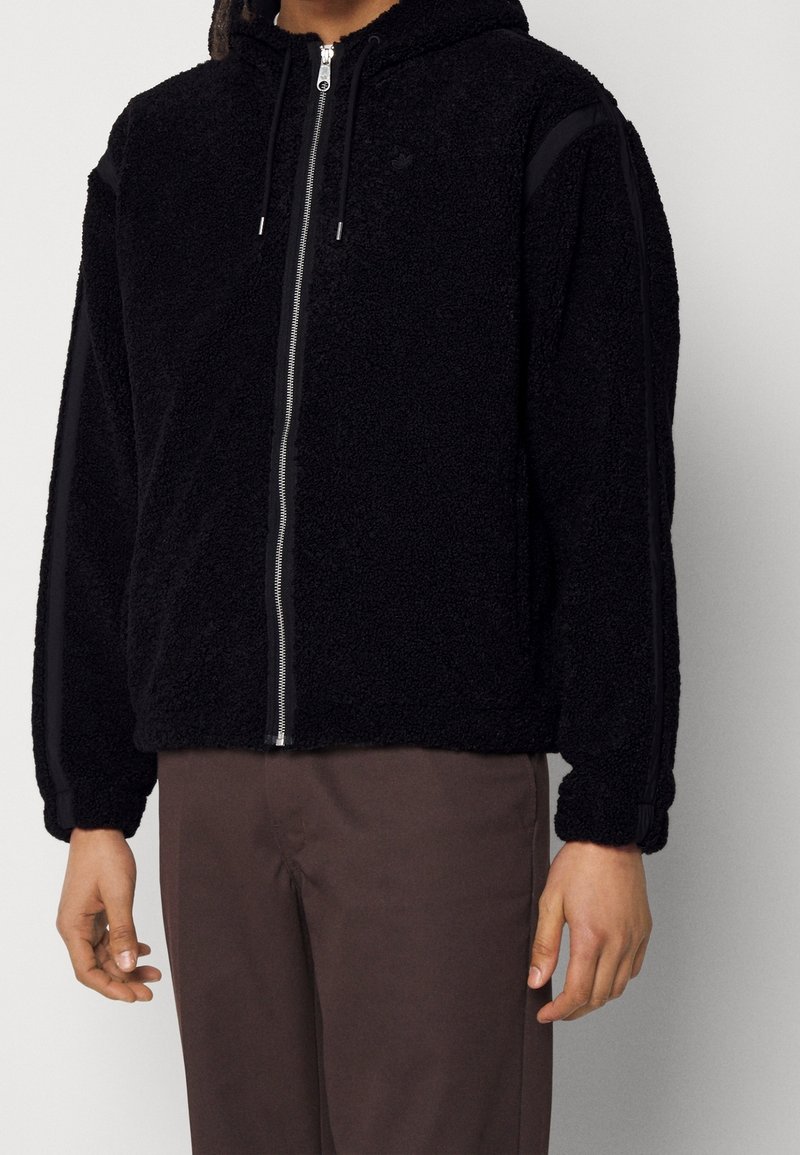 Schwarzer Fleece-Hoodie mit Reißverschluss vorne, verstellbarem Kordelzug an der Kapuze und schwarzen Seitenteilen; verfügt über eine strukturierte Stoffoberfläche und eine lockere Passform.