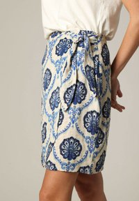 Wikkelrok van lichte stof met een crèmekleurige achtergrond en blauwe bloemenpatronen, met een strikdetail in de taille.