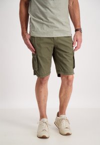 Pantaloni cargo verde oliva con tasche laterali, realizzati in un tessuto resistente. Indossati con una maglietta grigia chiara e sneakers beige.