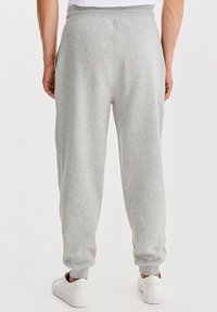 Szare bawełniane spodnie dresowe o luźnym kroju, z elastycznym pasem i mankietami; widoczne boczne kieszenie; w połączeniu z białymi trampkami.