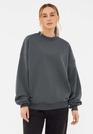 Gray oversized sweatshirt with a ribbed collar and cuffs. Soft texture, relaxed fit, and dropped shoulders. Paired with black pants.