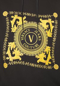 Felpa nera con cappuccio caratterizzata da una grande e complessa grafica dorata con un cerchio di catene e motivi floreali, che mostra "Versace Jeans Couture."