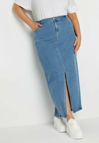 Vaaleansininen farkkumaksihame, jossa on etuhalkio, korkea vyötärö ja sivutaskut, yhdistettynä valkoisiin lenkkareihin.