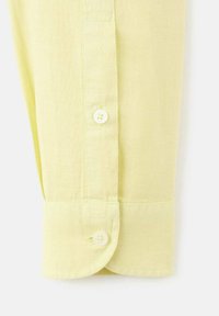 Puño de camisa de lino amarillo claro con cierre de botón, textura sutil y diseño de puño redondeado.