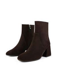 Bottines en daim marron avec un talon épais, un bout pointu et une fermeture éclair sur le côté. Texture douce avec des lignes lisses et épurées.