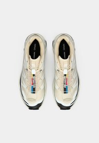 Μπεζ αθλητικά παπούτσια με διαπνέον επάνω μέρος από δίχτυ, λευκές λεπτομέρειες και μαύρη σόλα. Διαθέτουν σύστημα γρήγορου δέσιματος και λογότυπο στη γλώσσα και στην πλευρά.