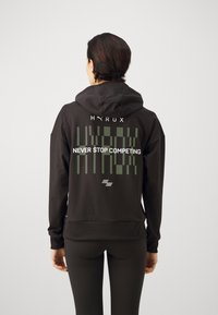 Schwarzer Hoodie mit lockerer Passform, bedruckt mit grütem Grafiktext "HYRUX" und "NEVER STOP COMPETING" auf dem Rücken. Weicher, strukturierter Stoff, Kängurutasche.