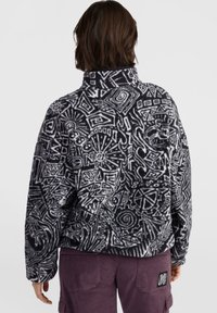 Pull en polaire noir et blanc avec des motifs abstraits et un col montant. Présente une coupe décontractée et une surface texturée.