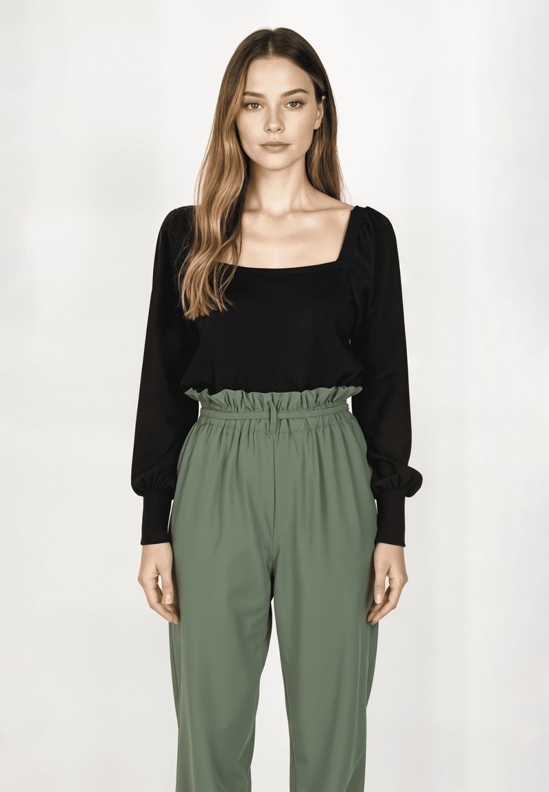 Top negro de manga larga con escote cuadrado y mangas abullonadas, combinado con pantalones verdes de talle alto que tienen cinturilla elástica y una textura suave.