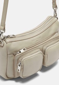 Beżowa skórzana torebka crossbody z wieloma zamykanymi na zamek kieszeniami, gładką fakturą i srebrnymi akcentami. Kompaktowy design, wszechstronne zastosowanie.