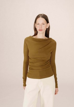 Haut à manches longues vert olive avec décolleté drapé et design ajusté, fabriqué en tissu côtelé. Le mannequin le porte avec un pantalon crème. Texture lisse.