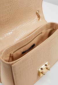 Beige väska med krokodilmönster och slät yta, guldfärgad hårdvara och ett innerfack med dragkedja. Rektangulär form med magnetstängning.