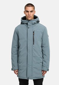 Ljusblå isolerad parkas med huva, framtida dragkedja och tryckknappar, dragkedjeförsedd bröstficka, elastiska ärmslut och sydda detaljer på tyget.