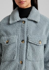 Fuzzy blue jacket made of textured fabric, featuring two front pockets, a collar, and brown buttons for closure.