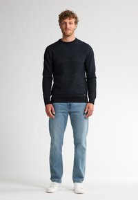 Marineblauw gespikkelde gebreide trui met geribbelde manchetten en halslijn. Gecombineerd met lichtblauwe jeans en witte sneakers. Effen achtergrond.