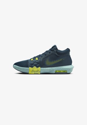 Chaussure de basketball Nike bleu foncé avec des touches jaunes, texture matelassée près des lacets, et une semelle bleu clair tachetée avec un amorti à air visible.