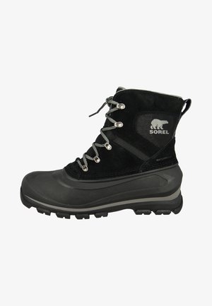 Bota de invierno impermeable negra con suela de dibujo grueso, cordones grises, ojales de metal y logo de Sorel con un oso polar en el tobillo.